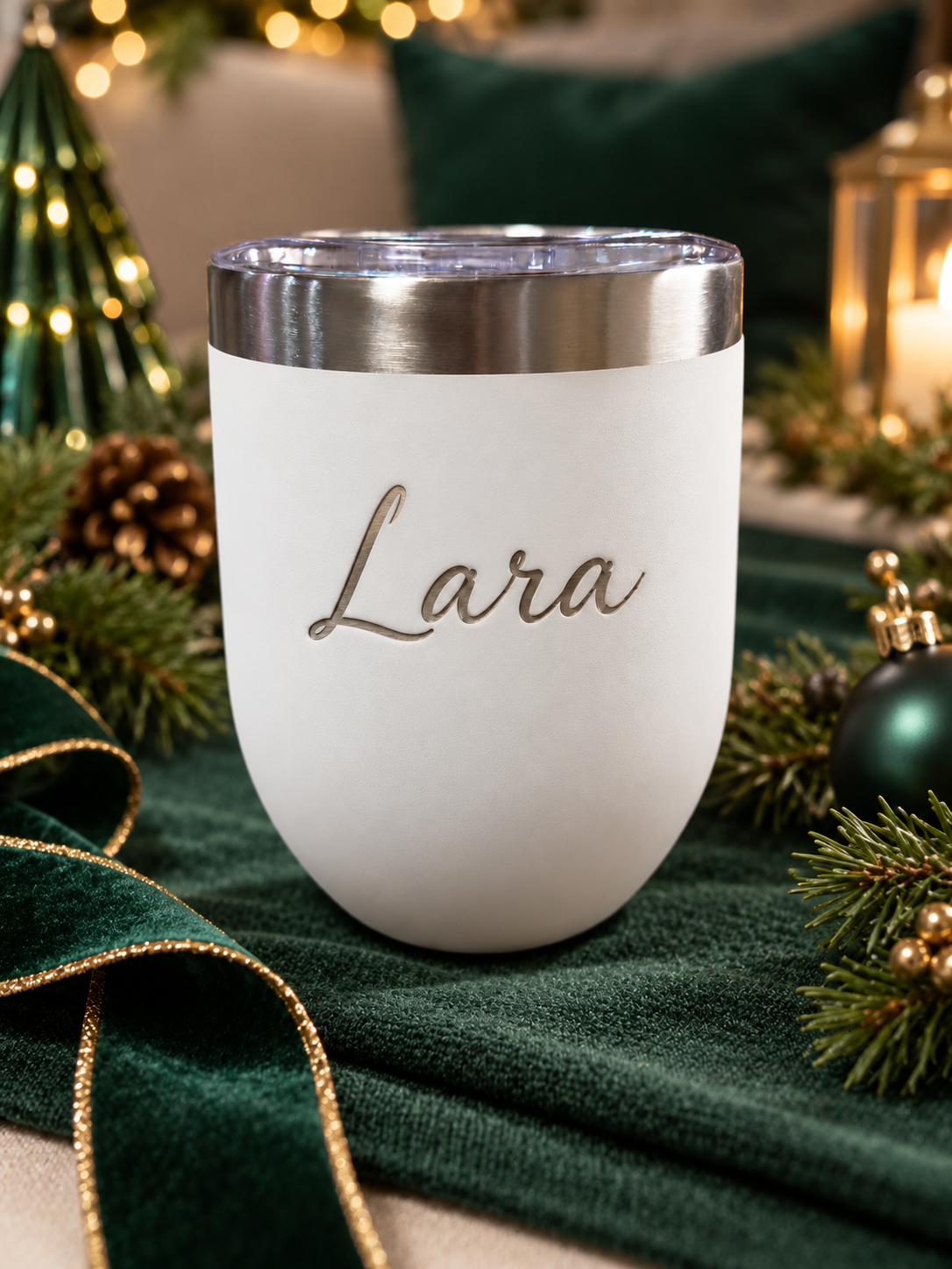 Personalised white insulated tumbler with the name Lara, displayed on emerald green velvet with festive Christmas decorations by The Collective Nook.